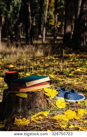 Books, Mug Of Coffee Or Tea, Laceless Denim Sneakers And Yellow Fallen Leaves On A Stump In The Autu