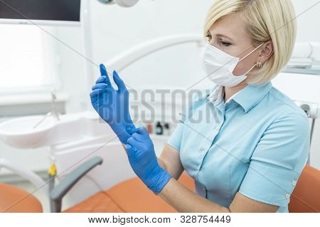 Young Blonde Female Dentist Adjusting Medical Gloves In Her Cabinet