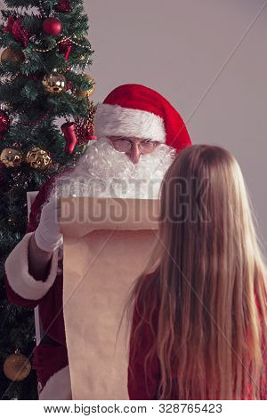 Santa Claus With With List Or Nice Or Naugthy List Paper With Small Girl Near Christmas Tree