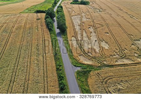 Aerial Drone Perspective On Damaged Wheat Field After Wind Storm, Rural Landscape With Asphalt Road.