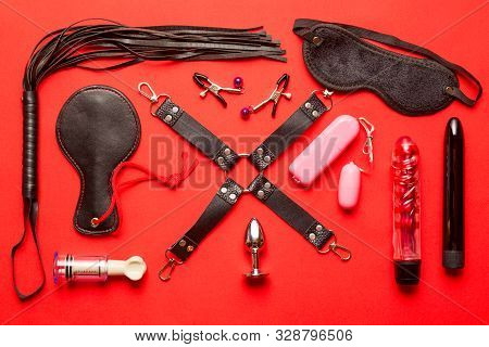 Bdsm Kit From Sex Shop. Leather Whip, Buttplug, Vibrator, Dildo, Nipple Clamps And Other On Red Back