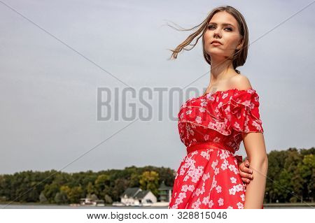 Portrait Of A Beautiful Young Brown-haired Girl With Long Hair In A Red Dress On A Lake Background.