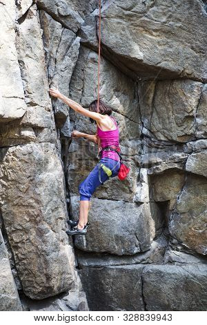 The Girl Climbs The Rock. Rock Climber Is Training On Natural Terrain. Extreme Hobby. A Woman Overco