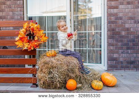 Adorable Laughing Caucasian Baby Toddler In White Knittes Jacket Sitting On The Haystack With Pumpki