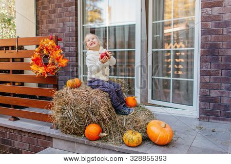 Adorable Laughing Caucasian Baby Toddler In White Knittes Jacket Sitting On The Haystack With Pumpki