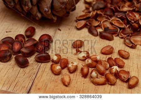 Cedar Nuts, Shell And Siberian Pine Cone. Peeled Kernels Lie On A Wooden Cutting Gloss Of Hevea.