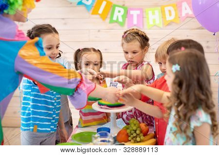 Clown And Children Group Gathered Together Around Festive Table. Childrens Holiday