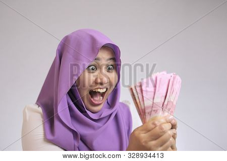 Portrait Of Indonesian Muslim Woman Holding Rupiah Money, Smiling Laughing Winning Gesture