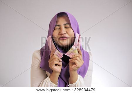 Portrait Of Indonesian Muslim Woman Holding Rupiah Money, Smiling Laughing Winning Gesture