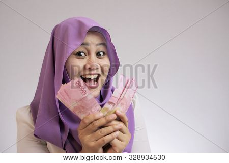 Portrait Of Indonesian Muslim Woman Holding Rupiah Money, Smiling Laughing Winning Gesture