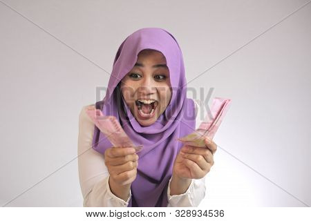 Portrait Of Indonesian Muslim Woman Holding Rupiah Money, Smiling Laughing Winning Gesture