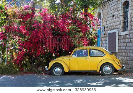 Nazaret, Israel - 14 June 2019: Yellow Volkswagen Beetle Vintage Car Parked In A Street Near Pink Bl