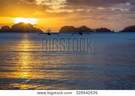 Couple Of Cruise Philippinean Bangca Boats Standing Still On Water With Sunset And Tropical Islands 