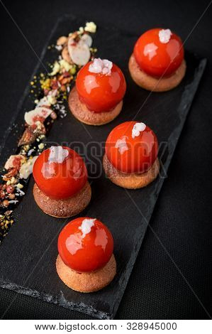 Mini Tartlets From Berries Glazed On Top Beautifully Laid Out On A Black Plate. Modern Dessert Festi