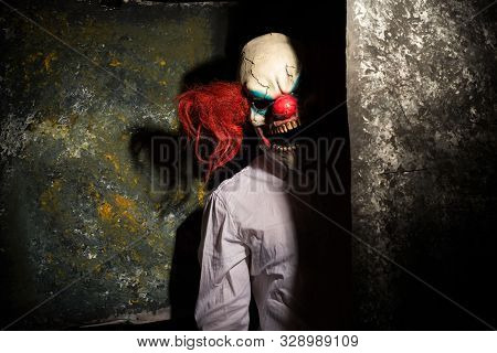 Scary Clown, In The Shadows, Looking Eerily At The Camera From Behind An Abstract Wall. Halloween Co