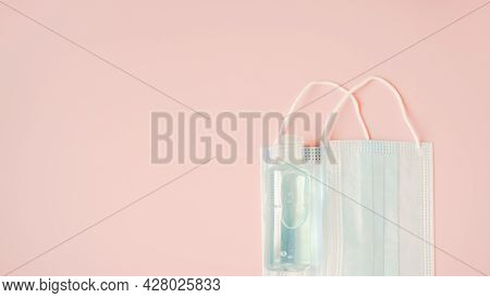 Two Medical Face Masks And Bottle Of Blue Alcohol Gel On Sweet Pink Background, Campaign For Wearing