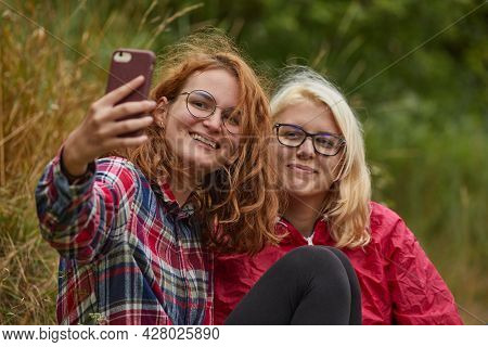 Girls taking selfies with a smartphone outoors in natural environment, focus on face on left