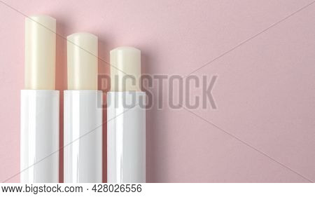 Top View Of Three Lip Balm Tubes On Pink Background.