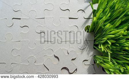Background Of The Cardboard Puzzle Without Pattern. Bright Green Grass Grows Through It On The Right