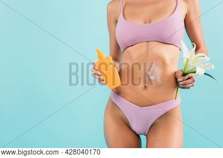 Cropped View Of Woman In Swimsuit Holding White Lily And Orange Bottle Of Sunscreen Isolated On Blue