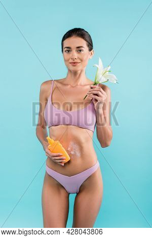 Slim Woman With Lily Flower And Sunblock Looking At Camera Isolated On Blue