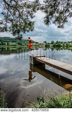 Rear View Of Man Jumping From Wooden Pier With Joy In To The Water,nature Reflected In Lake.having S