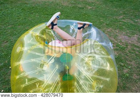 A Child In A Bumperball. Legs In Shorts Are Visible From An Inflatable Ball. Fun On The Summer Lawn
