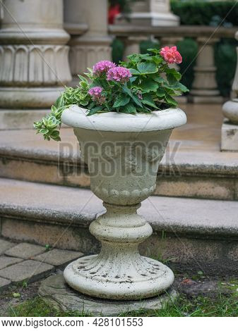 A Stone Bowl With Beautiful Red Flowers Near A Stone House. Cultivation Of Vegetation At Home.
