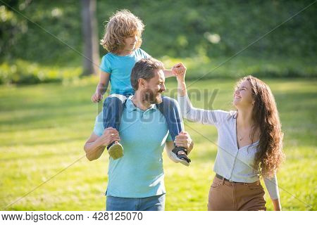 Happy Foster Family Of Mother And Father Carrying Adoptive Boy Child On Shoulders, Adoption.