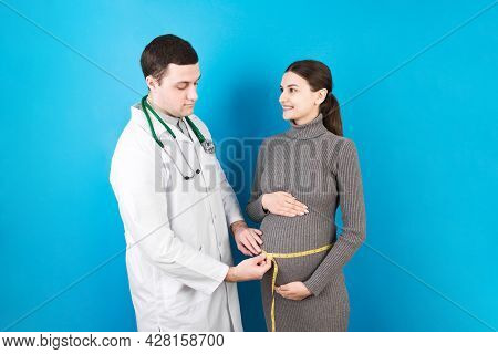 Happy Beautiful Pregnant Young Woman Touching Her Bare Tummy While A Doctor Is Measuring It
