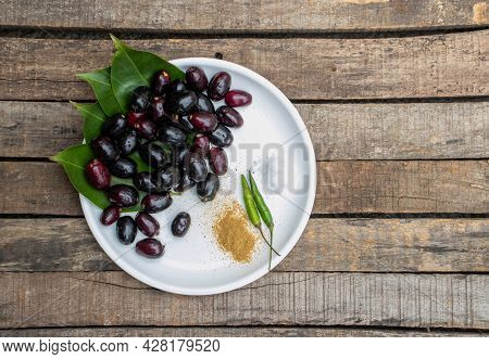 Top View Of Malabar Plum Or Jambolan In A Plate With Salt, Chili And Spices Isolated On Wooden Backg