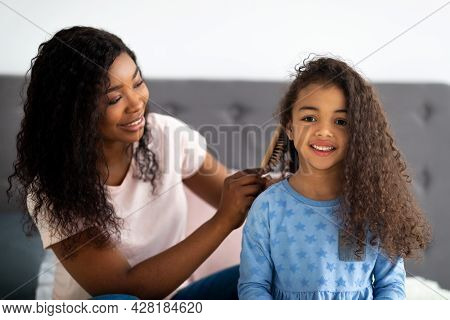 Beautiful Black Woman Brushing Her Daighters Hair On Bed Indoors