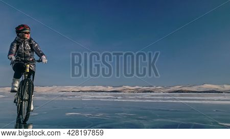 Woman Is Riding Bicycle On The Ice. Tires On Bike Are Covered Wi
