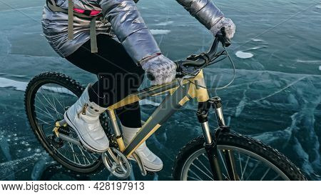 Woman Is Riding Bicycle On The Ice. Tires On Bike Are Covered Wi