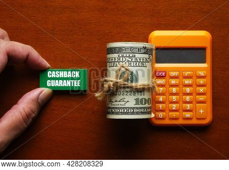 A Pictire Of Hand Holding Green Wood Written Cashback Guarantee, Fake Money And Calculator. It's A C
