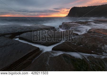 A Rocky Shore Next To A Body Of Water At Sunrise