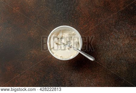Fresh Ricotta Cheese With Spoon In Package Bowl On Brown Background. Ricotta Soft Cheese On Old Tabl
