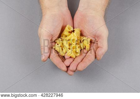 Campanelle, Gigli Or Ballerina Pasta. Dry Uncooked Pasta In Male Hands Against A Gray Background. Vi