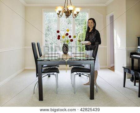 Mulher madura segurando pratos na sala de jantar