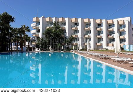 Hisaronu, Turkey - July 2021: View On The Swimming Pool And Empty Deck Chairs Against The White Hote