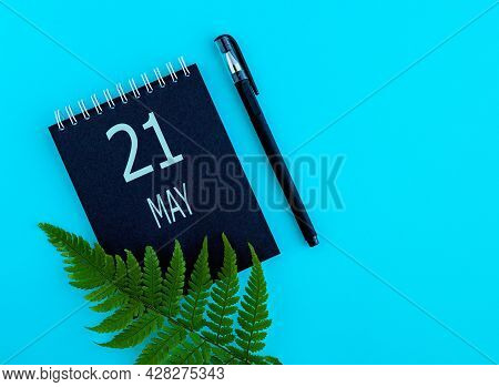 May 21th. Day 21 Of Month, Calendar Date. Black Notepad Sheet, Pen, Fern Twig, On A Blue Background.