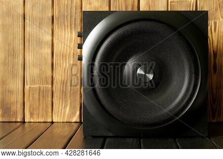 A Large Cube Subwoofer In A Wooden Case With A Metal Grill And Volume Controls Stands Against A Back
