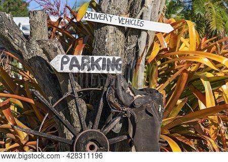 Hand Painted Signs On A Tree Above An Old Wagon Wheel And Disintegrating Saddle On A Country Propert