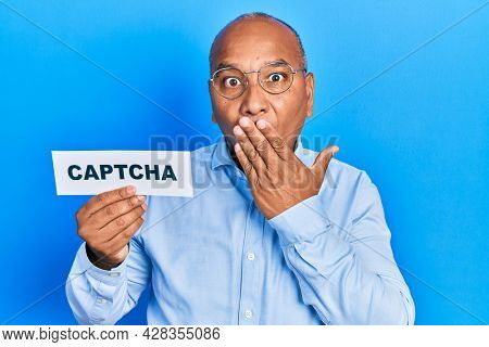 Middle age latin man holding captcha message paper covering mouth with hand, shocked and afraid for mistake. surprised expression 