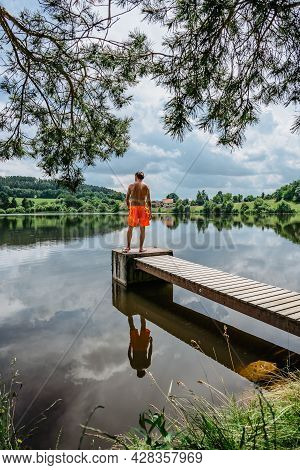 Rear View Of Man Jumping From Wooden Pier With Joy In To The Water,nature Reflected In Lake.having S
