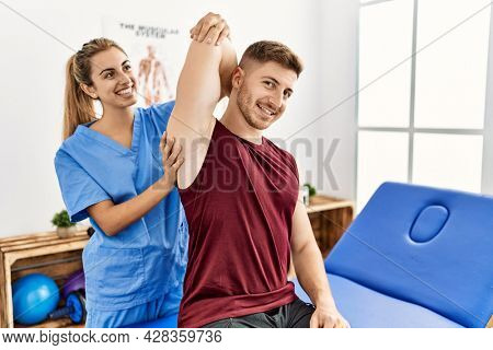 Young hispanic physioterapist woman make arm rehab treatment to man at the clinic.