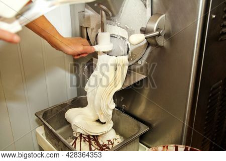 Female Worker Is Working On Ice Cream Maker Machine. Producing Vanilla Ice Cream With Chocolate Dres