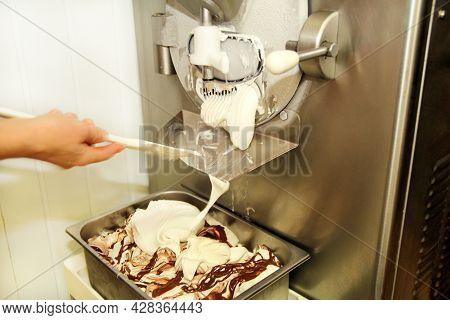 Female Worker Is Working On Ice Cream Maker Machine. Producing Vanilla Ice Cream With Chocolate Dres