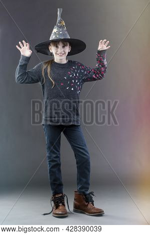 Little Girl In A Witch's Hat On A Gray Background. The Child At The Hallowin Festival.