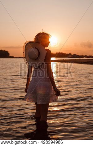 A Young Woman On The Background Of The Sunset. A Profile Picture Of A Beautiful Blonde In A White Dr